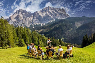 Degustazione di vini all'aperto in Alta Badia con vista panoramica sulle Dolomiti, guidata da un sommelier, circondati da prati verdi e montagne alpine.