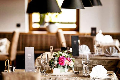 Tavoli elegantemente apparecchiati nel ristorante Rommisa a Vila di Sopra con tovaglioli in stoffa, calici e luce calda in un’atmosfera accogliente.