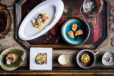 Menu Kosterle al Romantik Hotel Stafler: piccoli piatti gourmet presentati con eleganza su tavolo rustico, degustazione creativa con calice di vino.