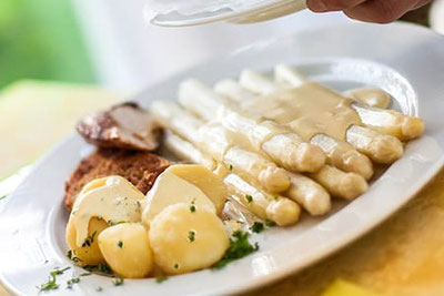 Teller mit weißem Spargel und cremiger Sauce, serviert mit Petersilienkartoffeln und knuspriger Beilage – typisches Gericht zur Spargelsaison in Südtirol.