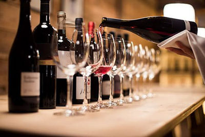 Un esperto di vini versa il vino Schiava in bicchieri, circondato da bottiglie di vini pregiati: una scena dal Trofeo Schiava al vigilius mountain resort.