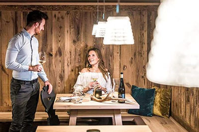 Una coppia si gode un bicchiere di vino nell'elegante ristorante Waldrast a Siusi allo Sciliar: arredi accoglienti in legno, luci calde e atmosfera romantica.