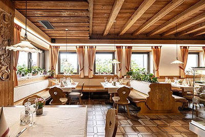 Accogliente ristorante altoatesino con soffitto in legno, panche tradizionali, tende decorative e tavoli apparecchiati con cura nella Garberstub a Parcines.