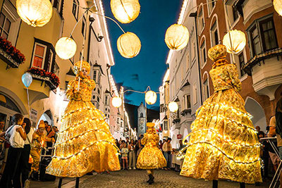 Figure luminose sui trampoli durante le Feste delle Lanterne di Vipiteno – atmosfera estiva, musica, spettacoli e fascino del centro storico.