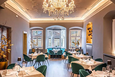 Elegante sala ristorante al Primo Piano a Bolzano: tavoli apparecchiati con stile, raffinate sedie in velluto, lampadari a braccio e cantinetta in un esclusivo locale per eventi nel cuore del centro storico.