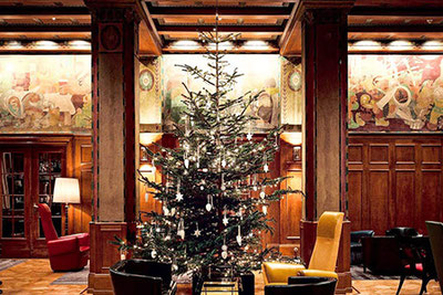 Weihnachtlich geschmückte Laurin Bar im Parkhotel Laurin in Bozen mit großem Christbaum, historischem Holzinterieur, bunten Wandmalereien und eleganten Sitzbereichen.