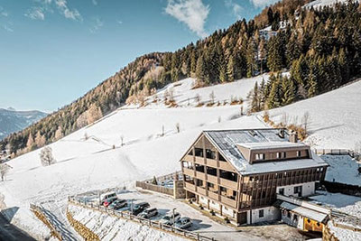 Restaurant Rommisa in Oberwielenbach bei Percha, modernes Holzgebäude in verschneiter Berglandschaft mit Parkplatz und Panoramablick im Pustertal.