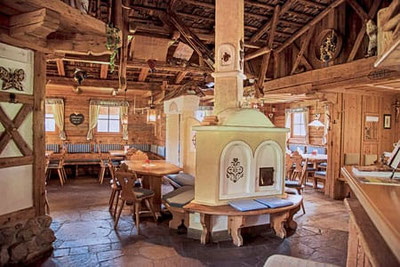 Traditionelle Stube im Restaurant Jora Mountain Dining in Innichen mit rustikalem Holzinterieur, gedeckten Tischen, warmem Licht und gemütlicher Alpenatmosphäre.