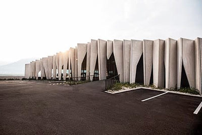 Moderne Fassade der Kellerei Kurtatsch in Südtirol mit skulpturalen Betonlamellen, klaren Linien und Blick auf die umliegenden Weinberge bei sanftem Morgenlicht.