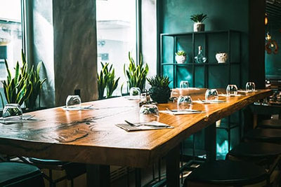 Modern eingerichtetes Restaurant Agorà 21 in Brixen mit stilvollem Holztisch, grünen Pflanzen und gemütlicher Atmosphäre – ideal für Tapas, Pizza und gutes Essen in Südtirol.