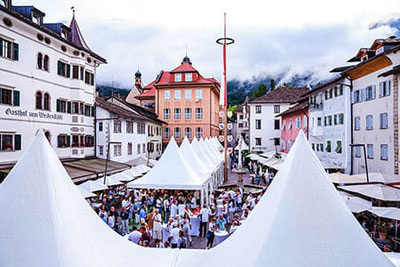 Der Marktplatz in Kaltern während der Veranstaltung „Kaltern ganz in Weiß“, mit festlich aufgebauten Zelten und einer großen Menschenmenge, die die besten Kalterer Weißweine verkostet und genießt.  
