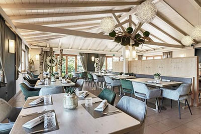 Ristorante Wiesenheim ad Appiano: sala da pranzo luminosa con un tocco alpino moderno, dettagli decorativi eleganti, sedie comode e grandi finestre con vista sul giardino.