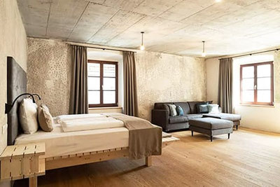 Großzügiges, stilvolles Zimmer im Rössl Bianco Hotel in Meran mit Holzboden, Designerbett, gemütlichem Sofa, Sichtbetondecke und charmantem Altbauflair.