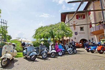 Bunte Vespas vor dem traditionellen Südtiroler Hof Hilberkeller beim Vespatreffen in Kuens – geselliges Event mit historischem Flair und regionaler Gastfreundschaft.