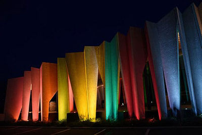 Facciata illuminata della Cantina Kurtatsch di notte: lamelle in calcestruzzo dai colori dell'arcobaleno risplendono suggestivamente durante l'evento “Aperitivo Panoramico” in Alto Adige.