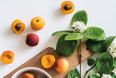 Albicocche fresche della Val Venosta su un tagliere di legno, accompagnate da foglie verdi e fiori, ideali per la Festa del Marmo e delle Albicocche a Lasa.