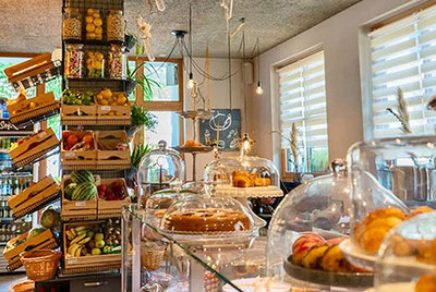 Interno del Postlodn di Stabner con frutta fresca, dolci sotto campane di vetro e un locale accogliente, un mix tra caffetteria, bar e negozio di specialità gastronomiche.