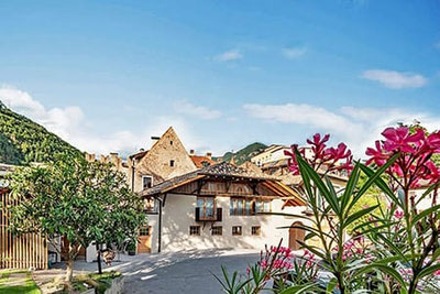 Weingut Schmid Oberrautner in Bozen-Gries mit historischem Gebäude, Innenhof, Holzbalkonen und blühenden Oleandersträuchern vor alpiner Kulisse.