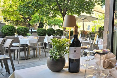 Tavolo elegantemente apparecchiato con vino rosso, bicchieri e decorazioni sulla terrazza del wine bar Gries 13 a Bolzano – ambiente raffinato sotto gli alberi in Piazza Gries.