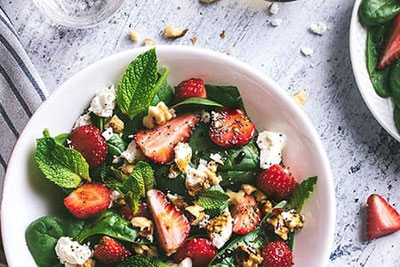 Insalata fresca estiva con fragole, spinaci, menta, noci e feta su piatto bianco durante la fresca estate nelle Locande Sudtirolesi.