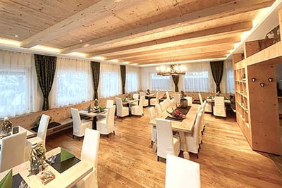 Sala luminosa del Ristorante Daimer a Campo Tures con pavimento in legno, tavoli apparecchiati, sedie bianche e atmosfera alpina accogliente.