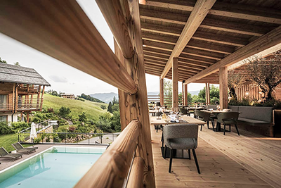 Blick in das Aparthotel Presulis in Völs am Schlern in Südtirol mit seiner in Holz gehaltenen Terrasse rechts und dem schönen Infinity Außenpool auf der linken Bildseite 