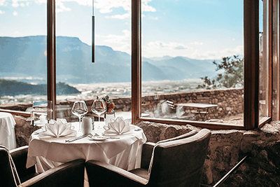 Tavola elegantemente apparecchiata con vista panoramica su Bolzano e sulle montagne dell'Alto Adige. L'elegante ambiente del ristorante Castel Flavon a Bolzano, in Alto Adige, unisce il piacere culinario a una vista mozzafiato.