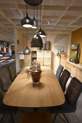 Esszimmer mit Holztisch, Stühlen und Pendelleuchten vor senfgelb-pastellfarbener Wand.