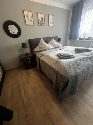 Gemütliches Schlafzimmer der Ferienwohnung „Auszeit am See“ mit Doppelbett, Nachttischen und stilvoller Wanddekoration. Warme Farbtöne, weiche Bettwäsche und liebevoll gefaltete Handtücher sorgen für eine entspannte und einladende Atmosphäre.