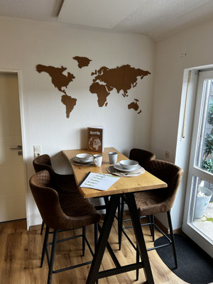 Moderner Essbereich in der Ferienwohnung „Auszeit Winterberg“ mit Hochtisch, bequemen Polsterstühlen und dekorativer Weltkarte an der Wand. Große Fenster sorgen für viel Licht – ideal für gemeinsame Mahlzeiten und gesellige Abende in Niedersfeld.