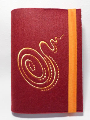 Stickmotiv Spirale in gelb-orangem Farbverlaufsgarn und Gummi in orangeauf bordeaux Filz (Filzfarbe fällt dunkler aus)