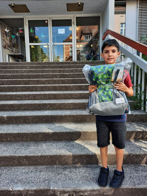 Ein Schüler steht mit seinem Gewinn in der Hand auf den Treppen vor dem Schulgebäude.