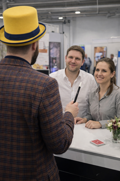 Magier Johannes zaubert auf einer Messe für zwei Zuschauer, Messebesucher
