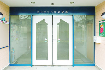 たけのパーク(集会所)入り口写真、右にポストと見取り図、中央は白い自動ドア、左には掲示板がある