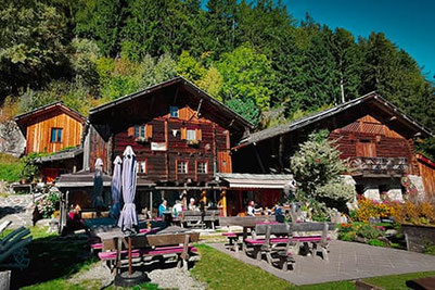 Gemütliche Jausenstation Naserhof im Kalmtal bei St. Martin in Passeier mit sonniger Terrasse, blühendem Garten und traditionellem Holzbau vor beeindruckender Bergkulisse.