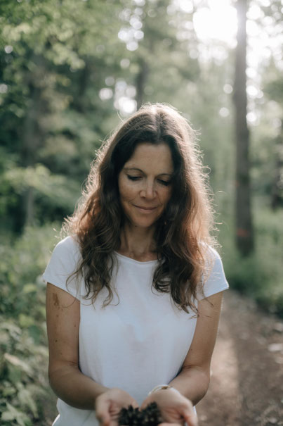 Petra Linner steht im Wald, blickt auf ihre Hände, in denen sie Erde hat