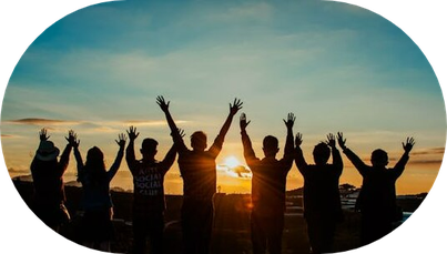 Gruppe, die Arme nach oben hebt vor Sonnenaufgang am Meer