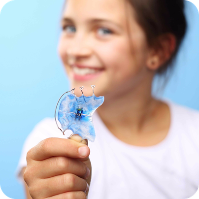 Lachendes Kind mit blauer herausnehmbaren Zahnspange in der Kieferorthopädie Gröbenzell.