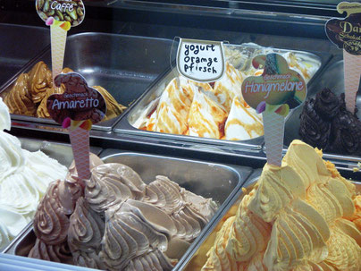 Sehenswürdigkeiten Aachen: Verschiedene Eissorten werden hinter einer Glasscheibe angeboten. Um die Auswahl zu erleichtern stecken in den unterschiedlichen Eissorten eine Anschrift wie «Amaretto» oder «Yogurt Orange Pfirsich».