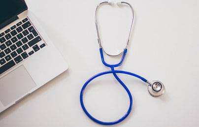 Ein Stethoskop liegt neben einer Tastatur, auf der Gesundheitstexte geschrieben werden.
