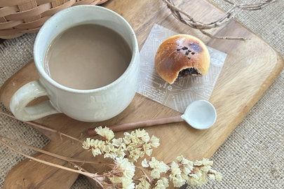 カッティングボードにのったカフェオレのマグカップとミニあんぱん。ドライフラワー。