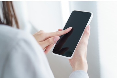 スマートフォンでネット予約をする女性の画像