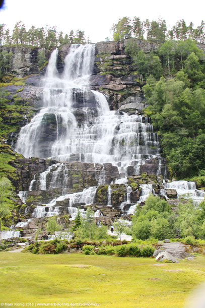 Trollafossen in full height: A lot of water falling over various cascades. A very small man in the photo illustrates the dimension of the fall.