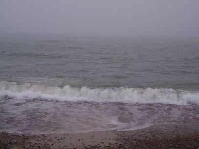 Die Nordsee im Nebel, im Vordergrund bricht sich eine Welle am Strand