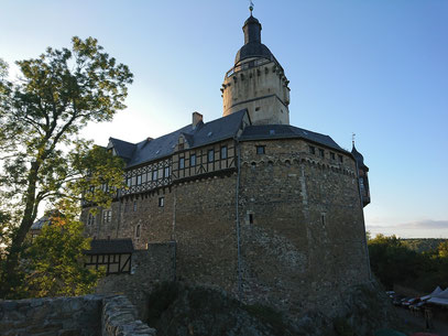 Burg mit hohen Außenmauern und einem Turm im Abendlicht