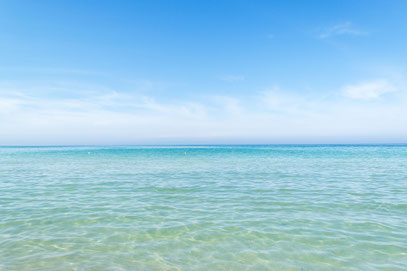 Bildausschnitt vom Meerwasser in Strandnähe, die Farbe ist vorne helltürkis und wird nach hinten dunkelblau. Der Himmel ist blau mit Schäfchenwolken.