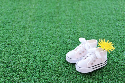 芝生の上にスニーカータイプのベビーシューズ。タンポポの花が添えられている。
