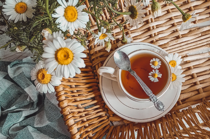 籐のトレイに載せられた紅茶のカップ＆ソーサ。ギンガムチェックのクロスとマーガレットの花。