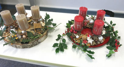 Fertig gestellte Adventskränze in Rot und Braun dekoriert und farblich passenden Kerzen bestückt.