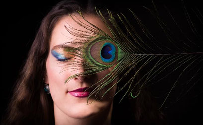 Nahaufnahme einer Frau mit Pfauenfeder vor dem Auge